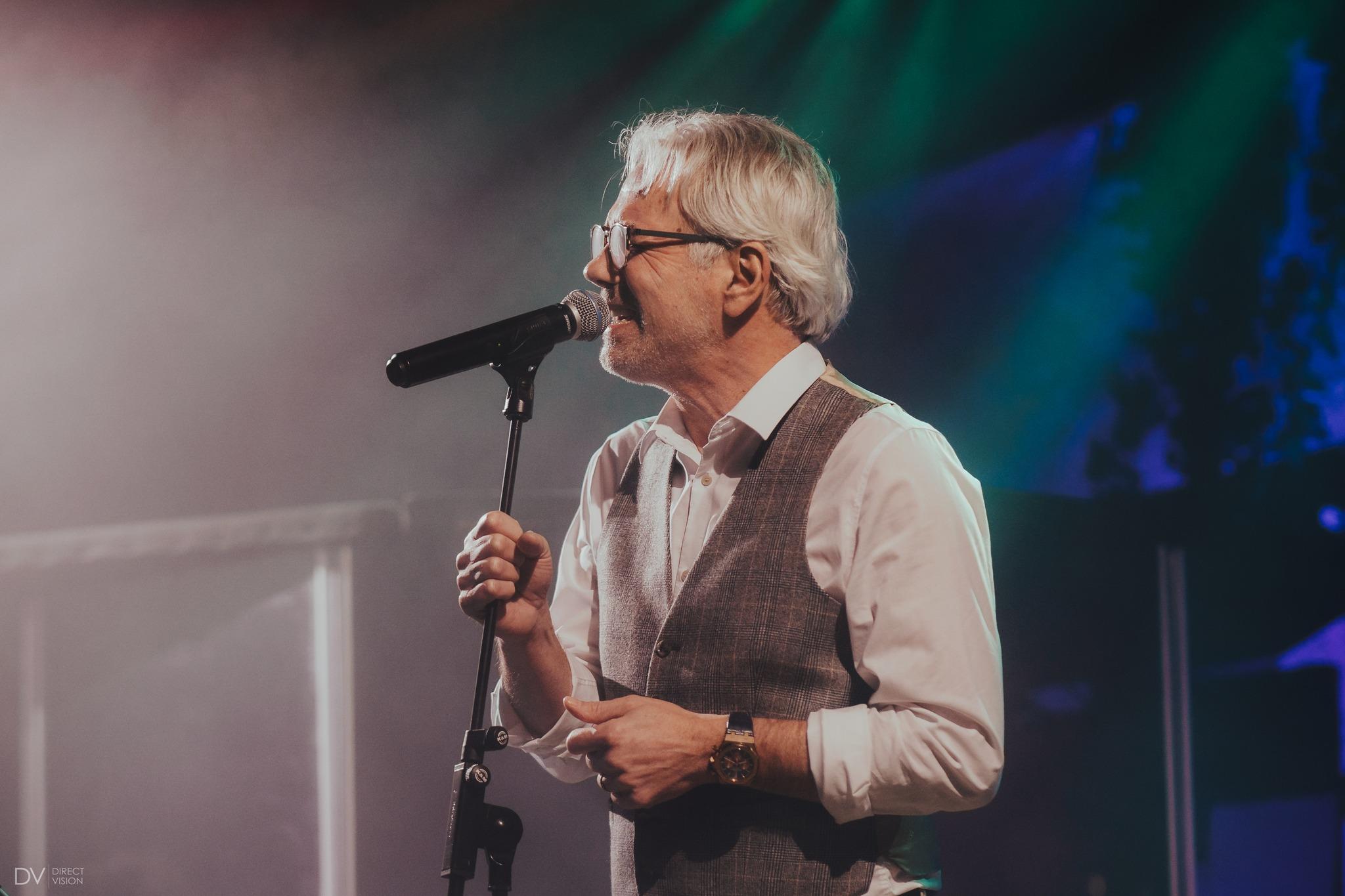 Robert Janowski sings into a microphone during a concert on stage.