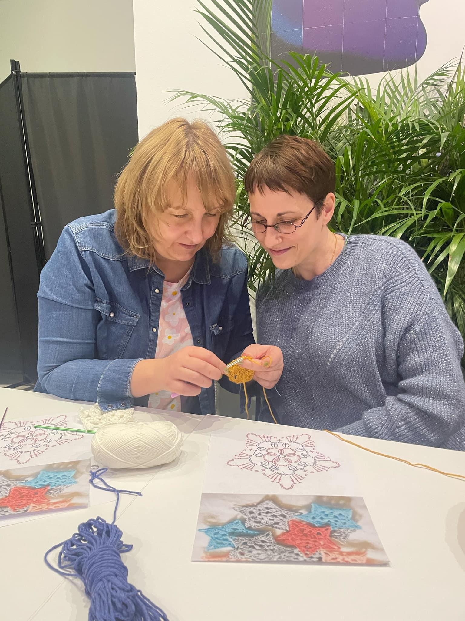 Participants in a handicraft workshop work on crocheting at a table.