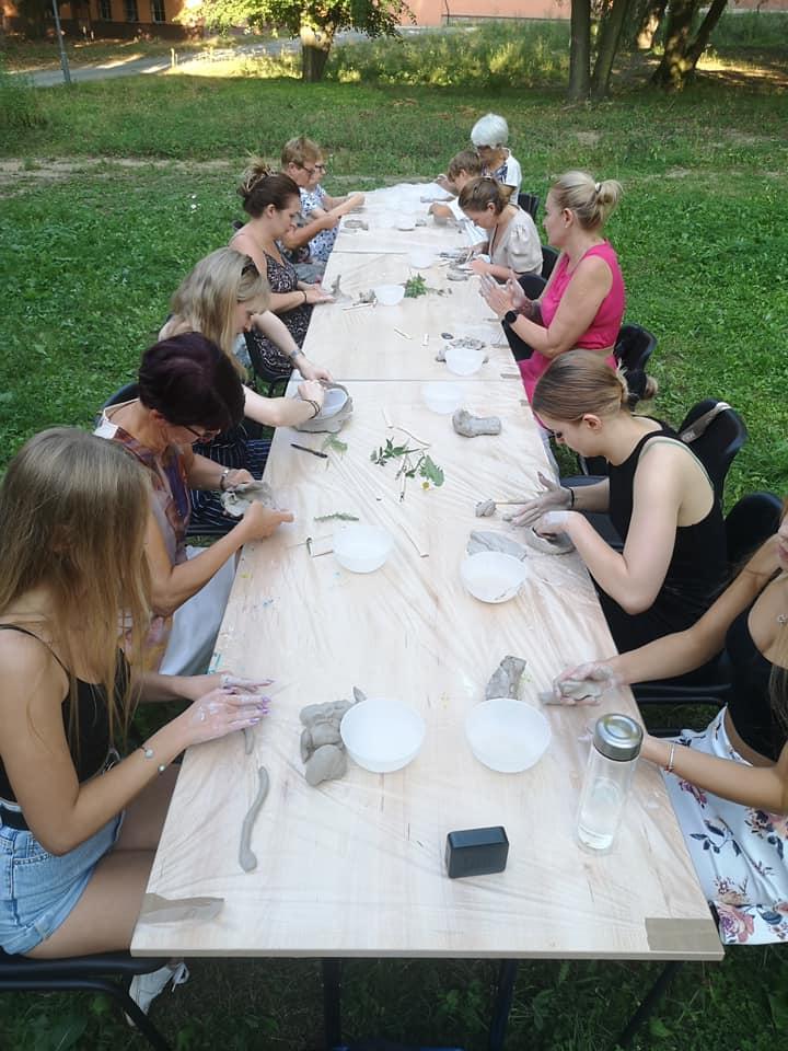Art class participants work at a shared table in a workshop space.