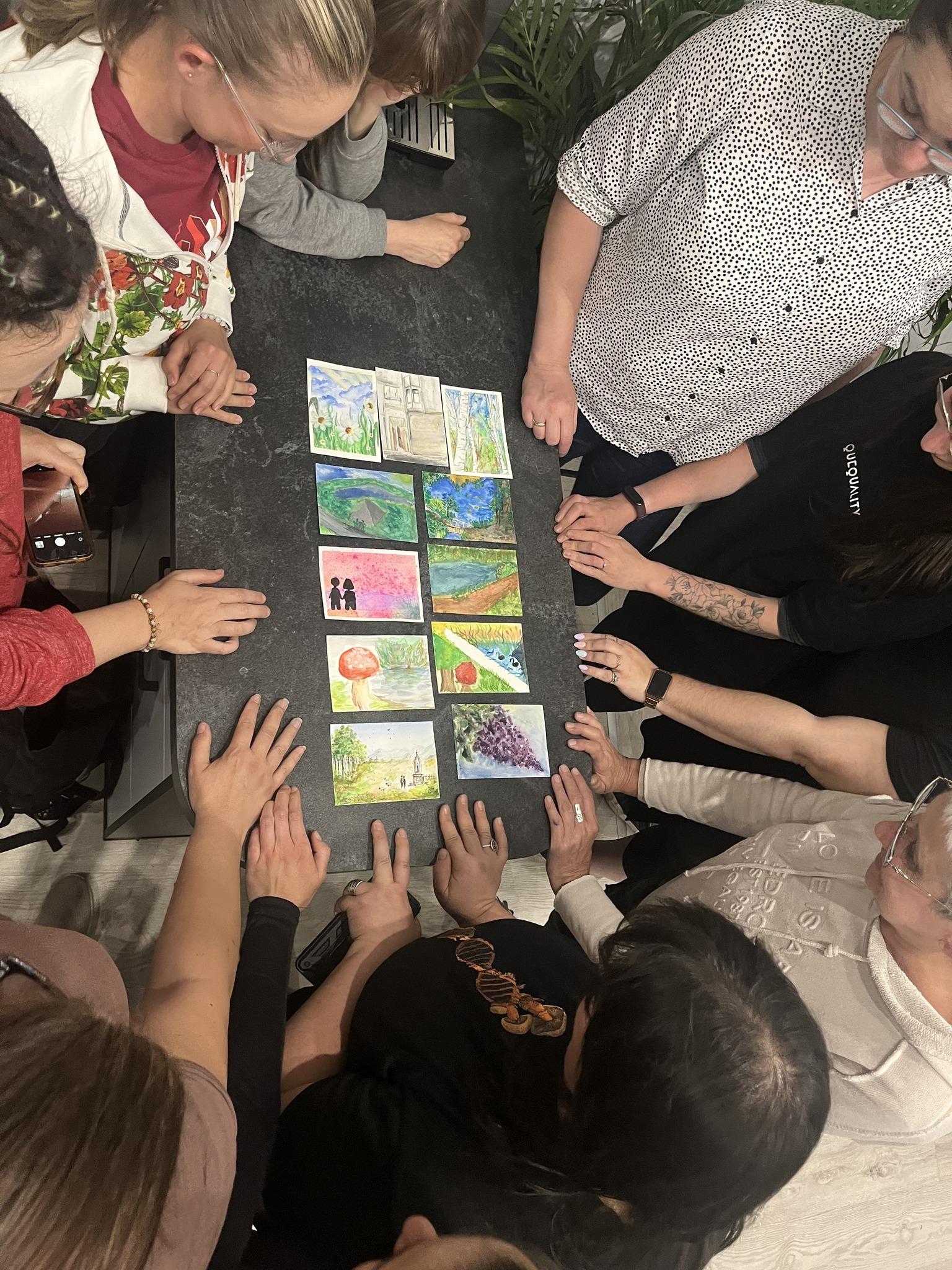 A group looks at and discusses a set of artworks laid out on a table.