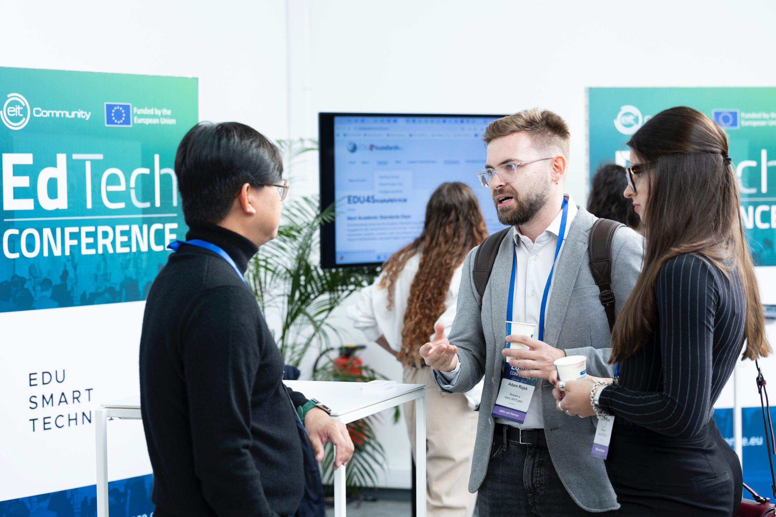 An attendee at the EIT EdTech 2025 conference talks with other participants at a booth in Brussels.